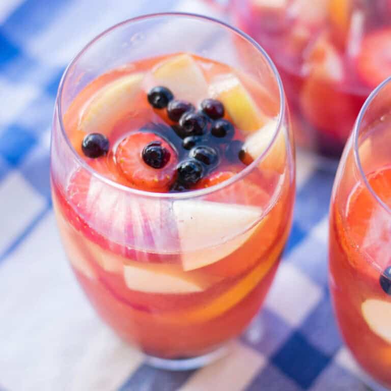 Two glasses of sangria with vodka and Rosé wine with sliced strawberries blueberries and apples on a blue checked tablecloth