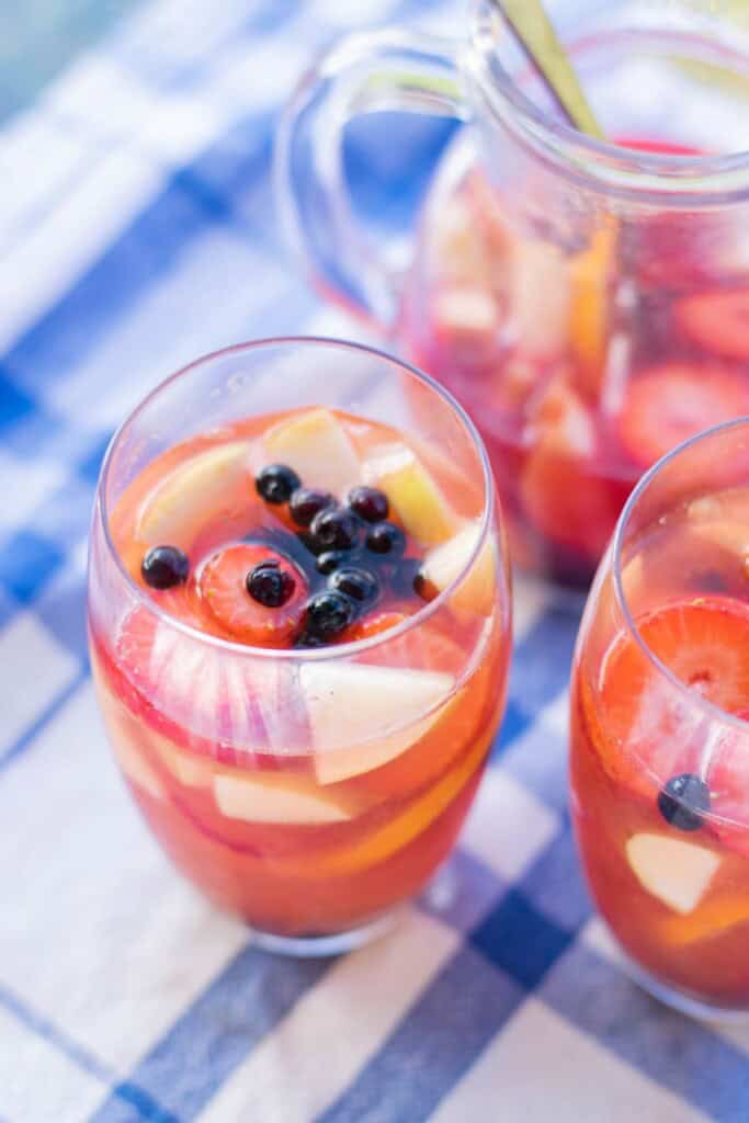 Two glasses of sangria with vodka and Ros&eacute; wine with sliced strawberries blueberries and apples on a blue checked tablecloth 