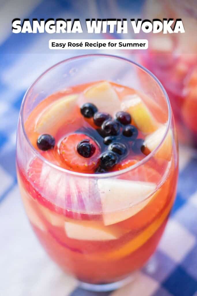 Pinterest pin for sangria with vodka recipe showing two glasses of Rosé sangria garnished with strawberries blueberries and apples on a blue checked tablecloth