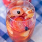 Tall glass of Rosé sangria with vodka filled with sliced strawberries blueberries and apple chunks ready to serve