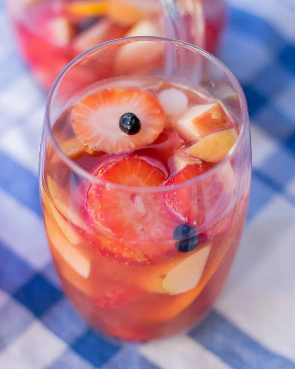 Tall glass of Rosé sangria with vodka filled with sliced strawberries blueberries and apple chunks ready to serve