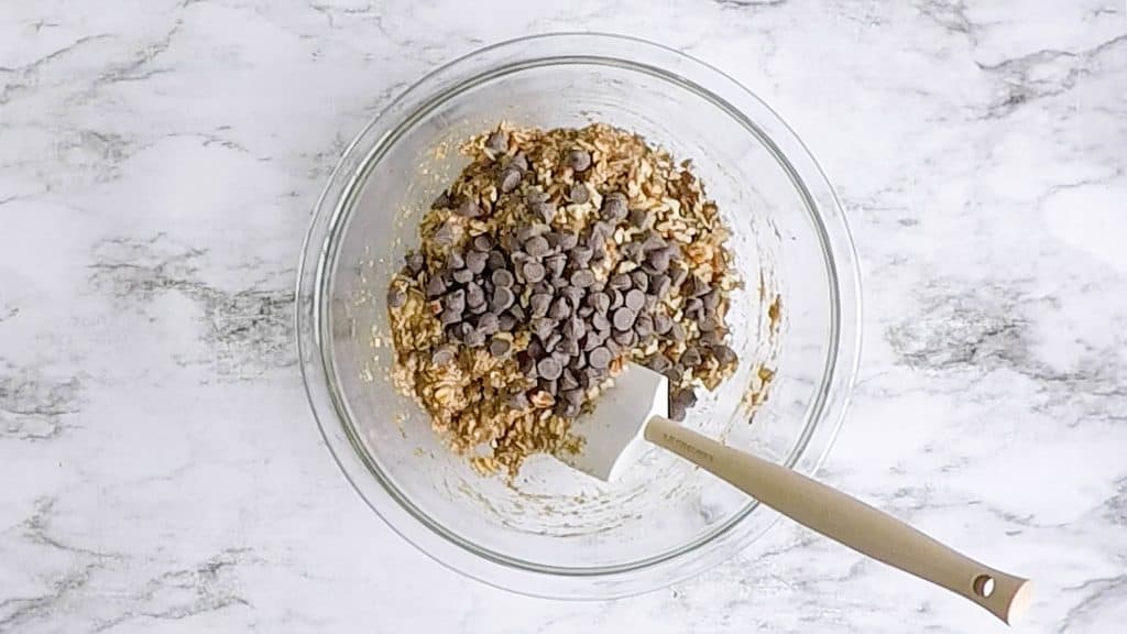 Chocolate Chips on top of cookie dough in a glass bowl with a spatula in it.