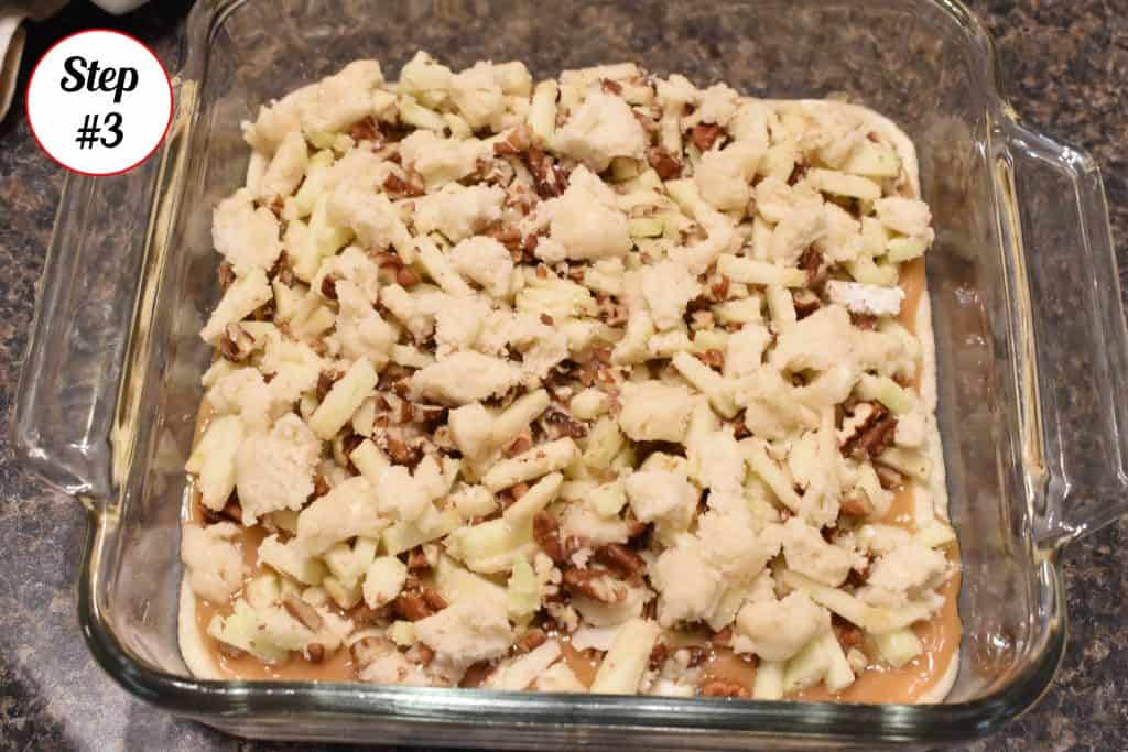 Apples and pecans on top of caramel and cookie dough in a glass baking dish.