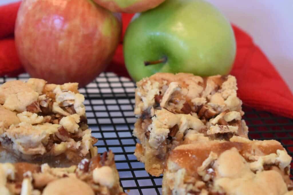 Caramel Apple Bars on a wire rack with apples in the background.