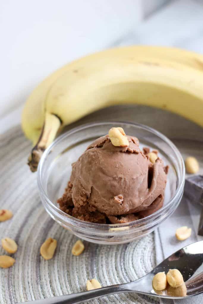 Peanut Butter Banana Chocolate Nice Cream in a glass bowl with peanuts on top and a banana on the side