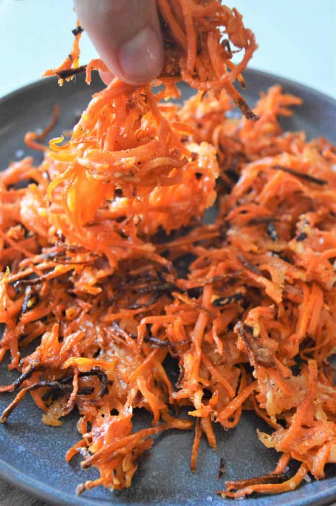 closeup of pinching together carrot fries off of a brown clay plate.