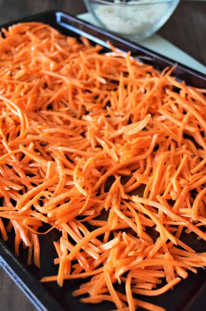 Shredded carrot on a black rimmed baking sheet.