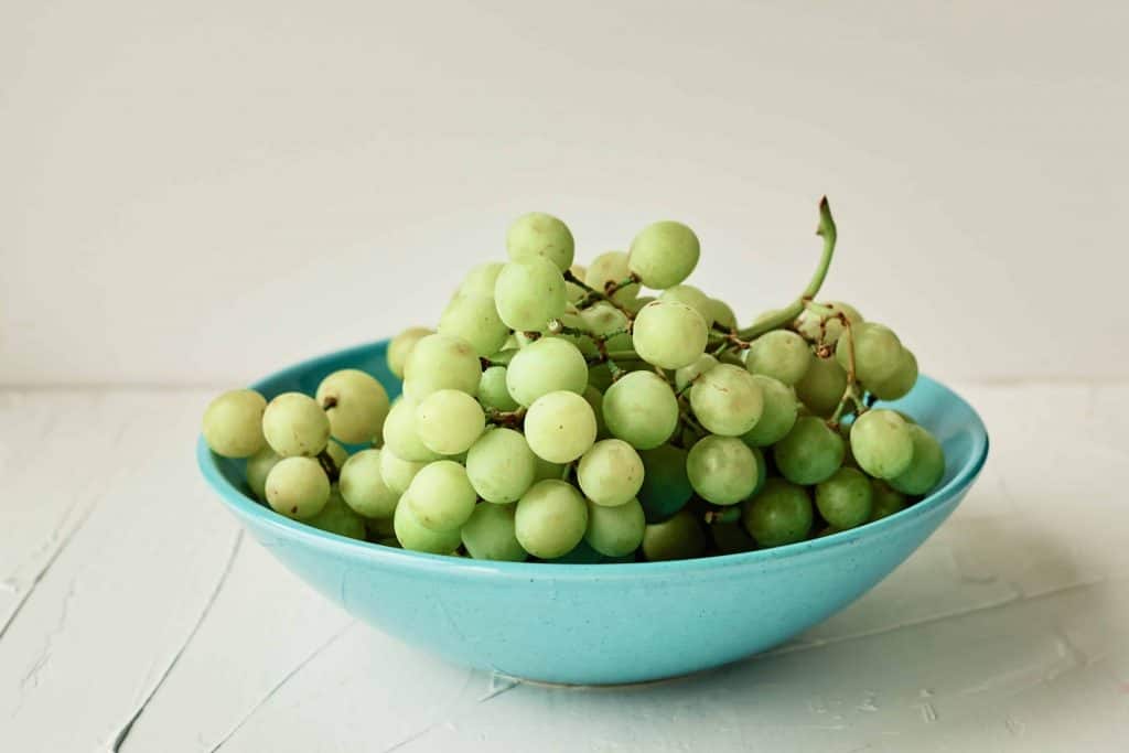 Green grapes in a blue bowl on a white background.