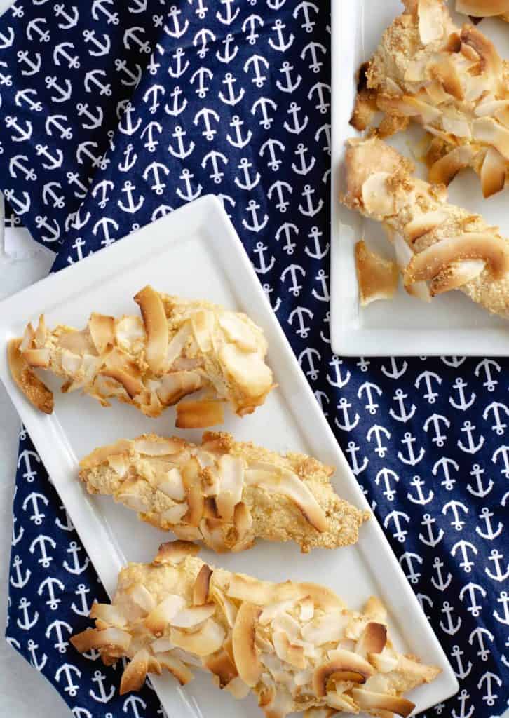 Keto Coconut Chicken Tenders on white plates with navy blue table cloth with anchors on it underneath.