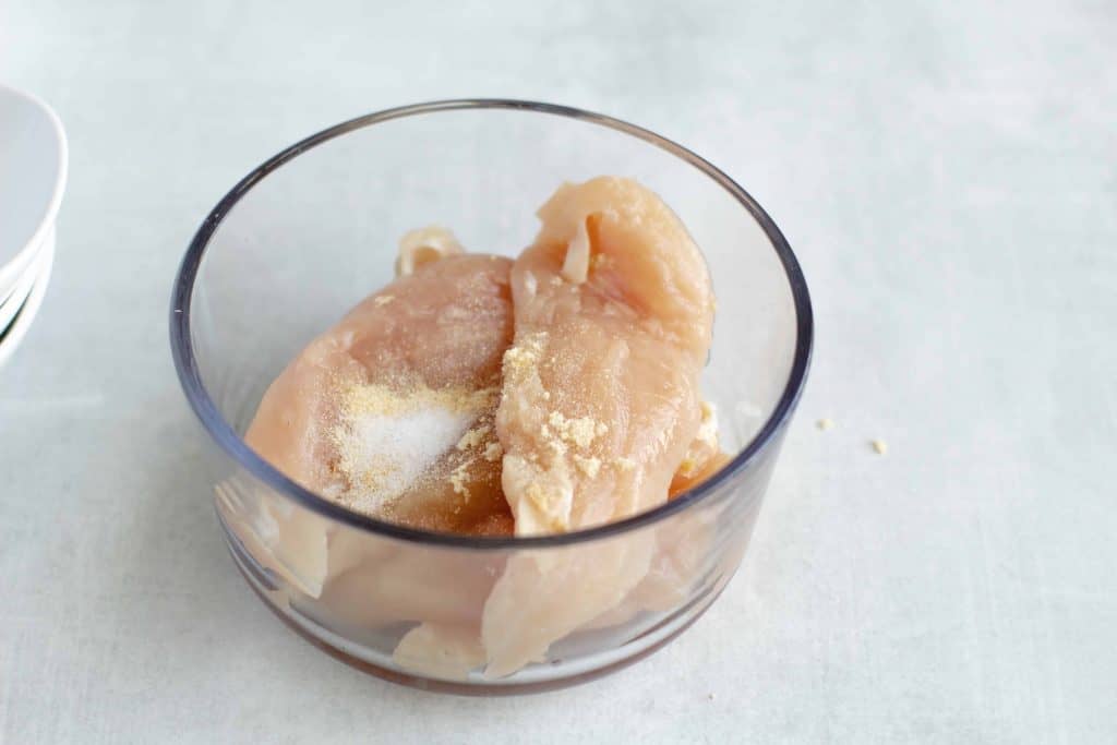 Chicken breast in a glass bowl with seasoning on top of it.