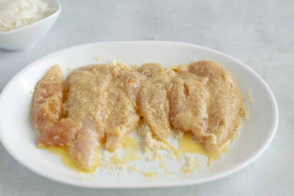 Chicken tenders on a white plate with breading and egg wash.