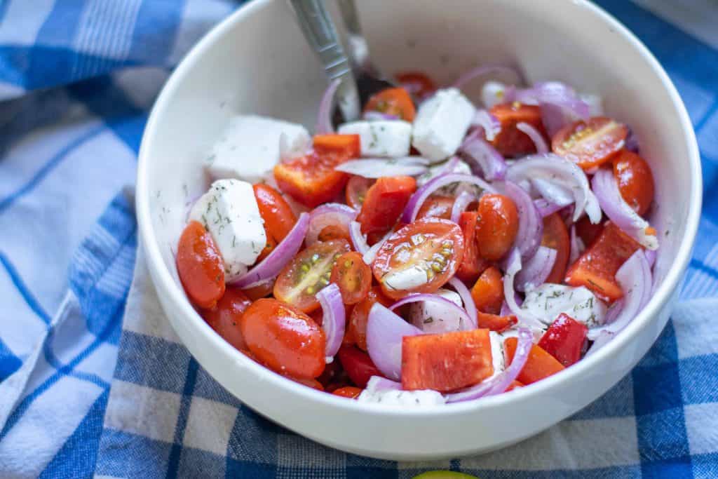 Closeup of Mediterranean Salad in a white bowl with a fork in it on blue checked table cloth