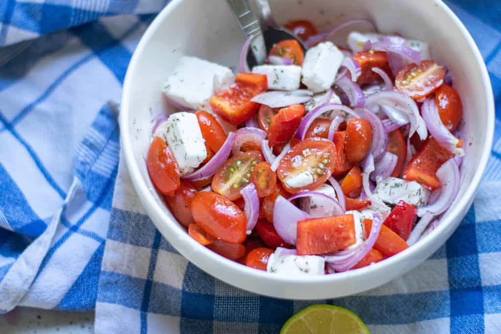 Overhead shot of tomato and feta salad on blue checked table cloth.