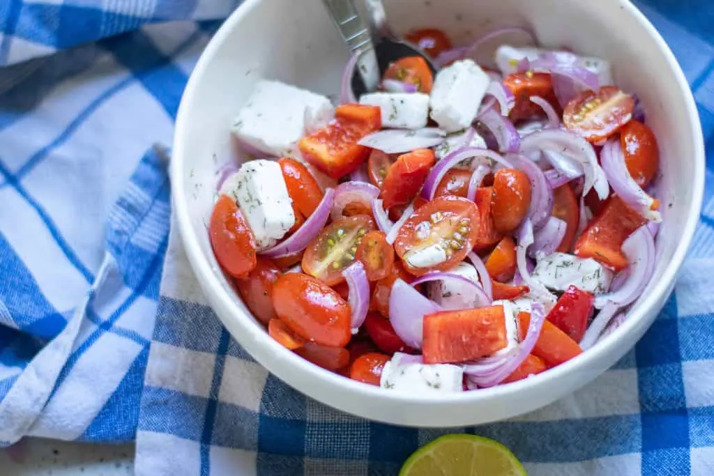 Overhead shot of tomato and feta salad on blue checked table cloth.