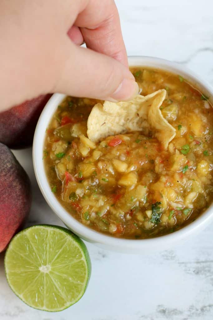 Overhead shot of chip in peach salsa with half of a lime beside it.