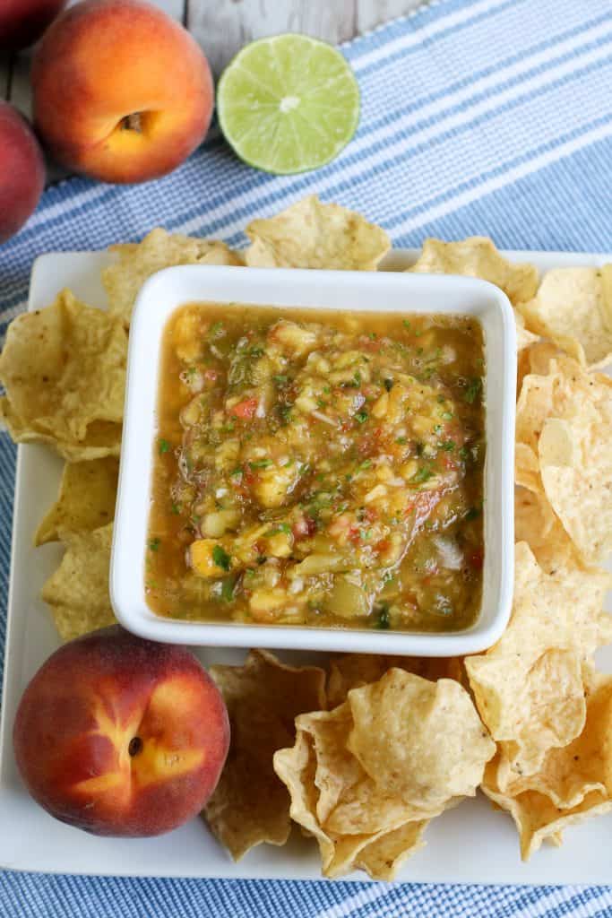 Overhead shot of peach salsa with chips an peaches around it on a white plate.