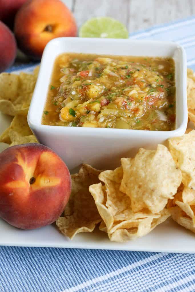 Fresh peach salsa on a white platter with a peach on it and tortillas chips.