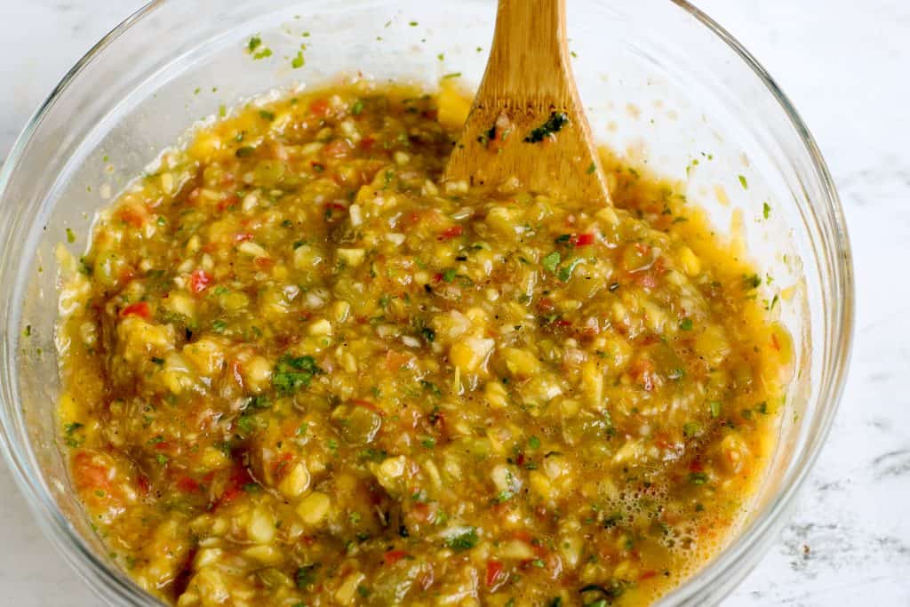 Peach salsa stirred in a large glass bowl with a wooden spoon in it.