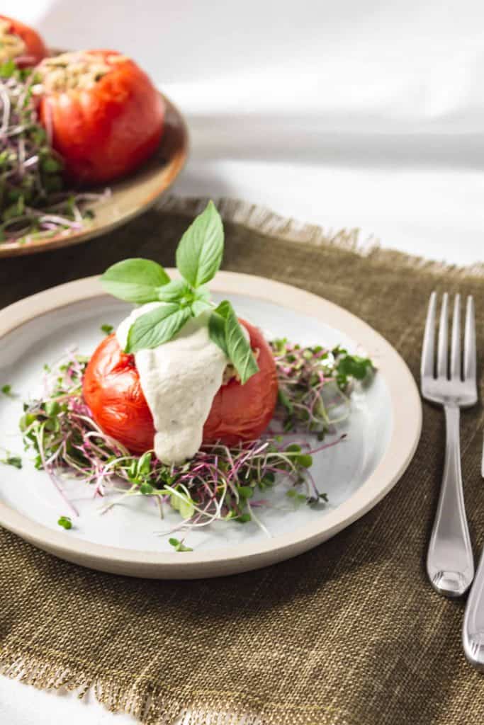 Rice stuffed tomato with cashew cream sauce and fresh basil on top served on a bed of micro greens.