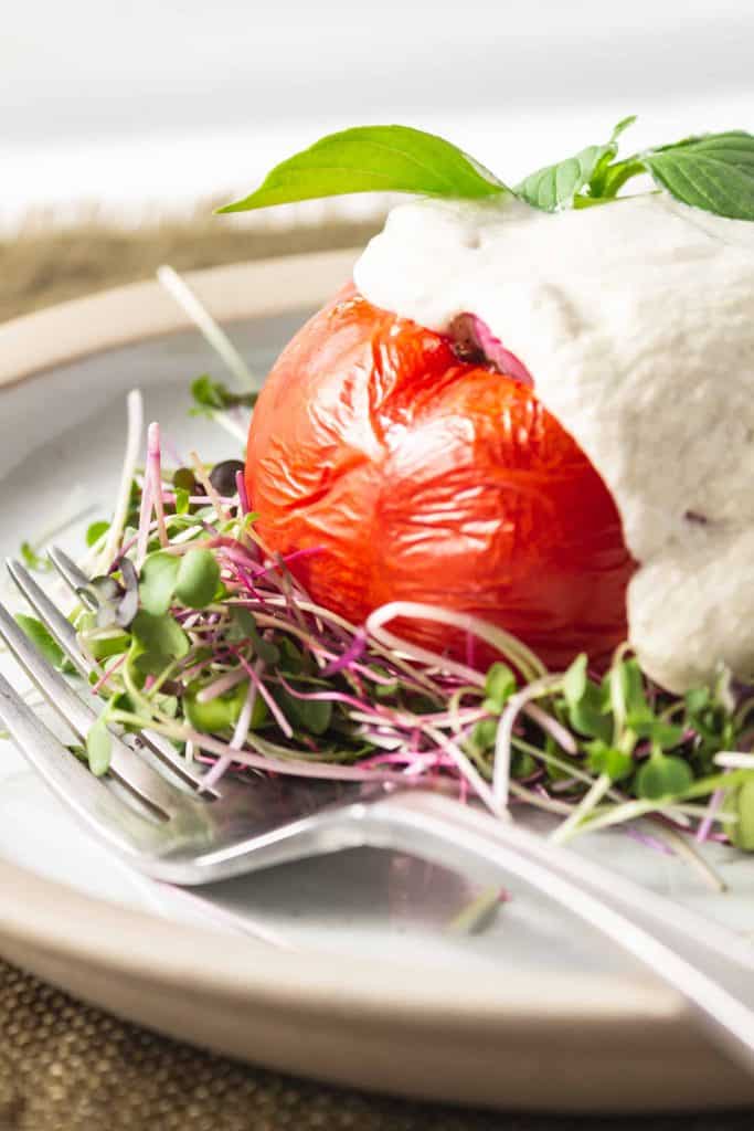 Tomato stuffed with rice and covered with cashew cream sauce on a bed of micro greens.