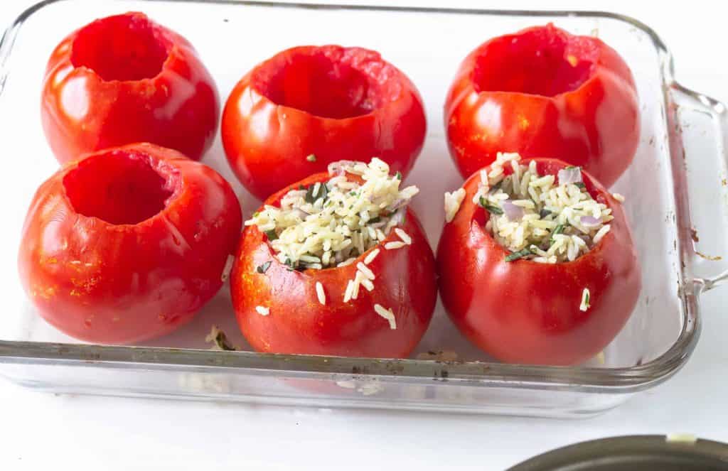 Glass baking dish with tomatoes inside of it, 2 stuffed with rice.