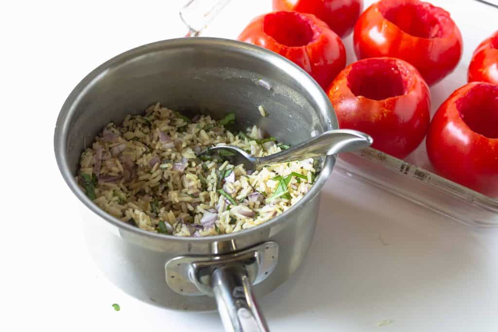 Rice in a sauce pan with pan of cored out tomatoes beside it.