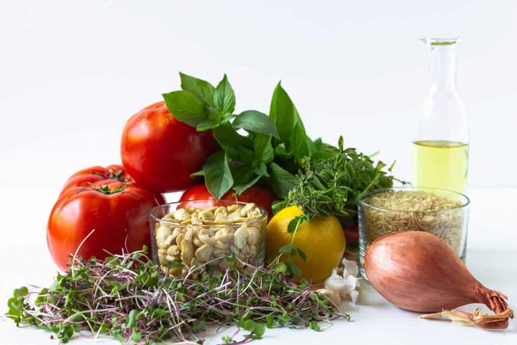 tomatoes, basil, olive oil, lemon, micro greens, cashews and a shallot on a white background.