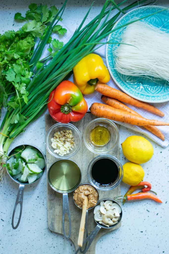 Overhead shot of bell peppers, carrots, green onions, fresh herbs, rice noodles and other fresh ingredients.