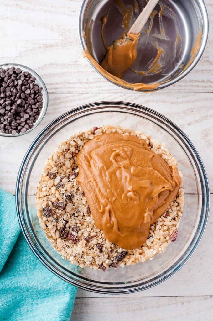 Oats and chocolate chips in a glass bowl with melted peanut butter on top and bowl of mini chocolate chips. in upper right corner.
