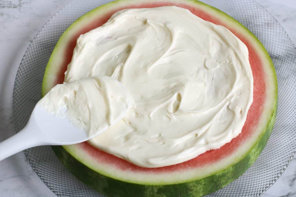 cream cheese icing being spread on slice of watermelon.