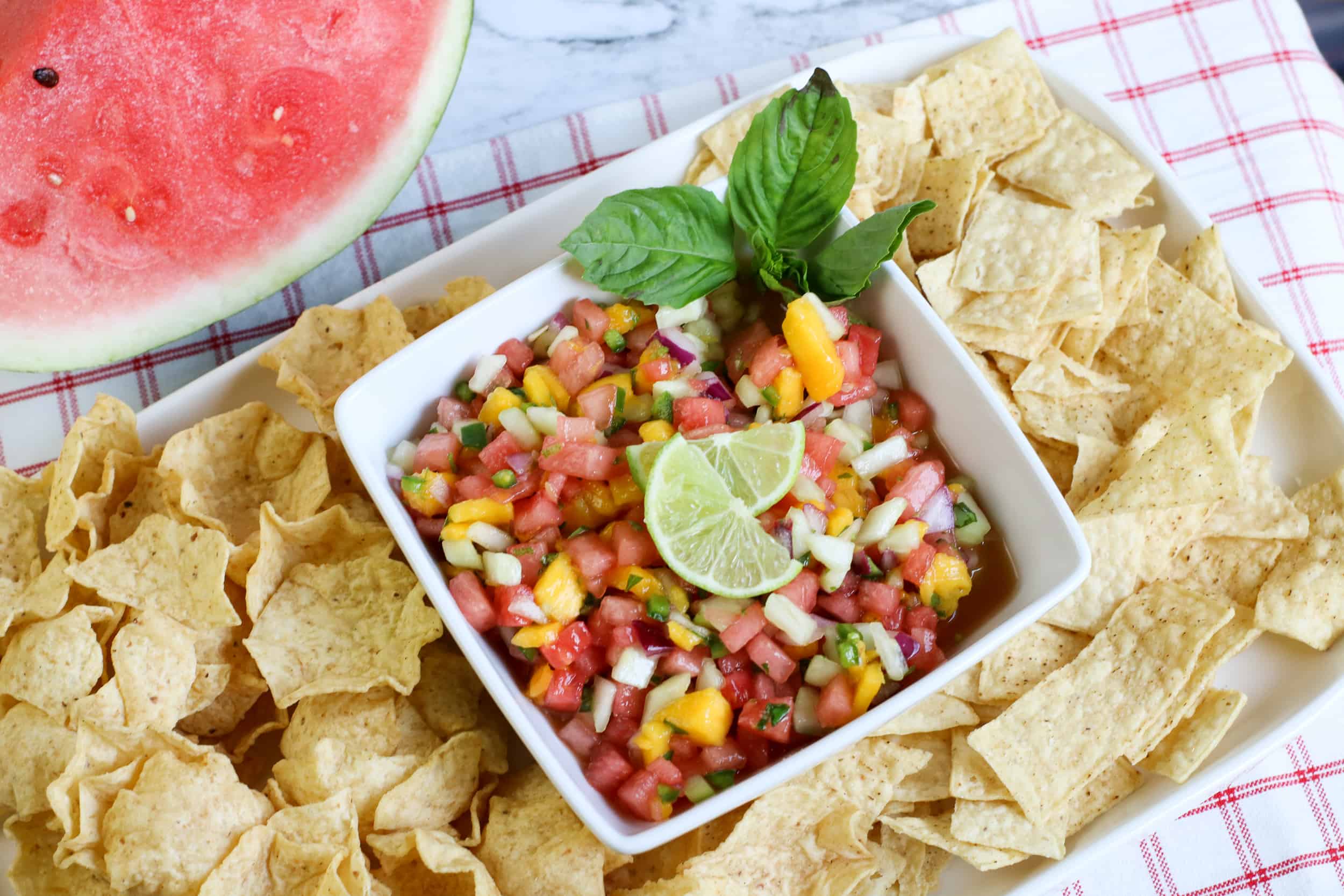Watermelon salsa in a white square dish with chips around it and a slice of watermelon on the side.