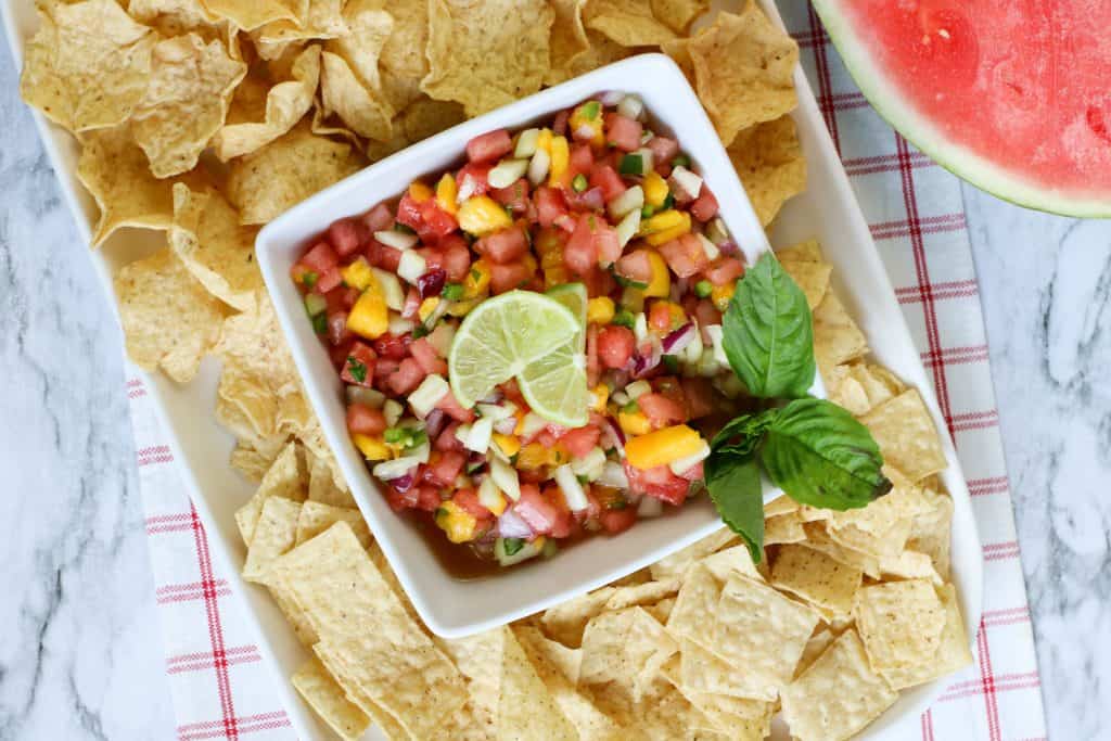 Fresh watermelon salsa topped with lime slices and mint surrounded by tortilla chip scoops.