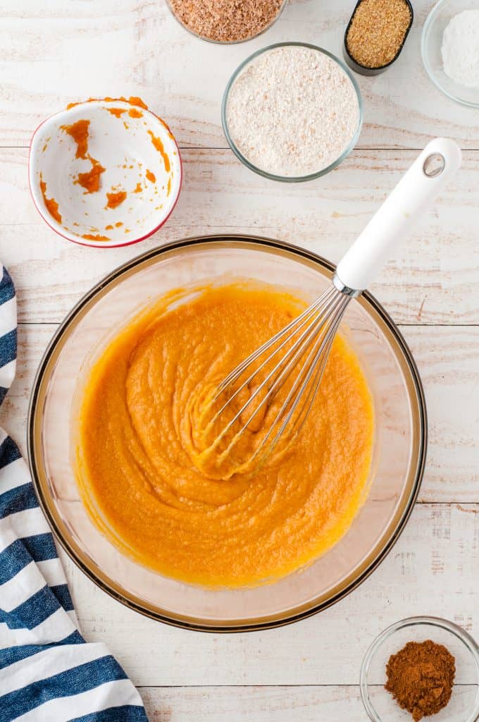 Pumpkin muffin batter in a glass bowl with a whisk in it.