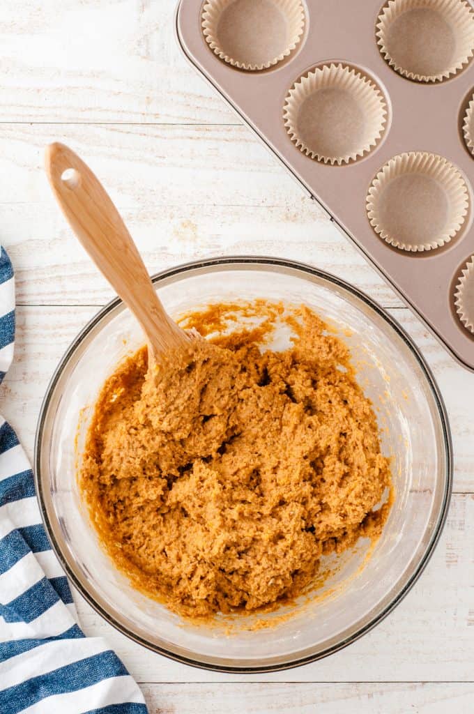 Whole wheat pumpkin muffin batter in a glass bowl with muffin tin in the corner.