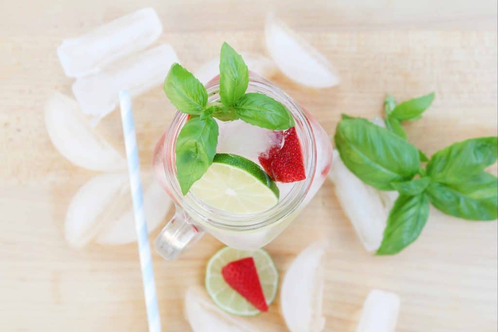 Overhead view of drink with strawberries, lime and basil surrounded by ice cubes.