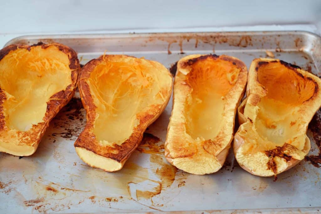 Butternut squash sliced in half and roasted on a baking sheet.