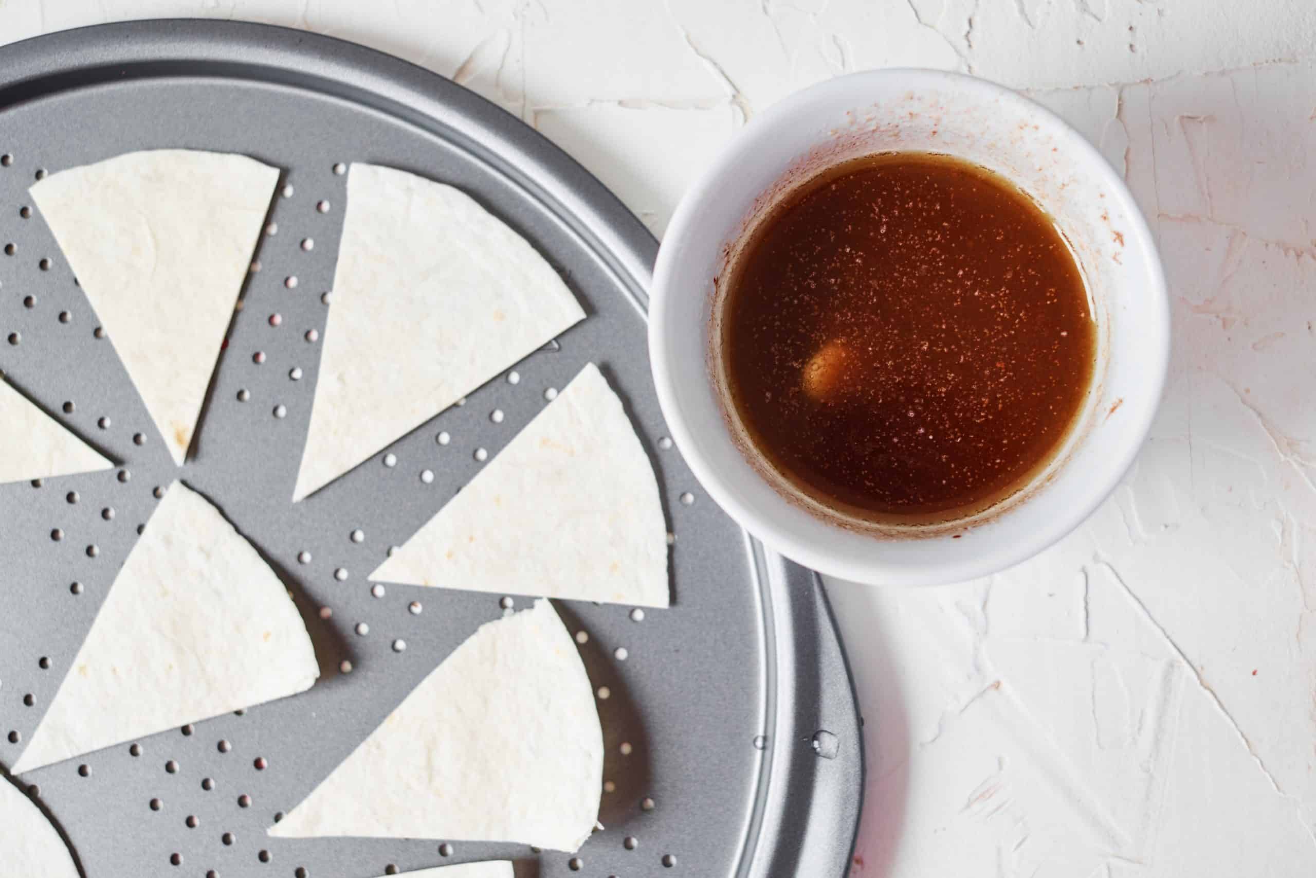 Tortillas on a baking sheet with butter, cinnamon and sugar mixture beside it on a white background.