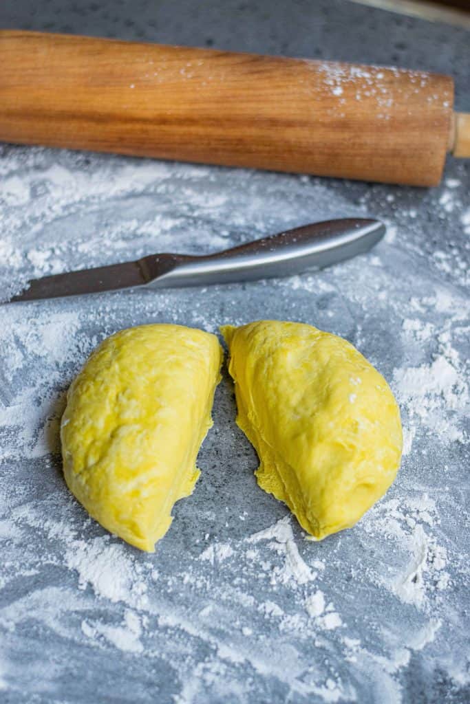 Homemade Pumpkin Pasta Dough cut in half on a floured surface.