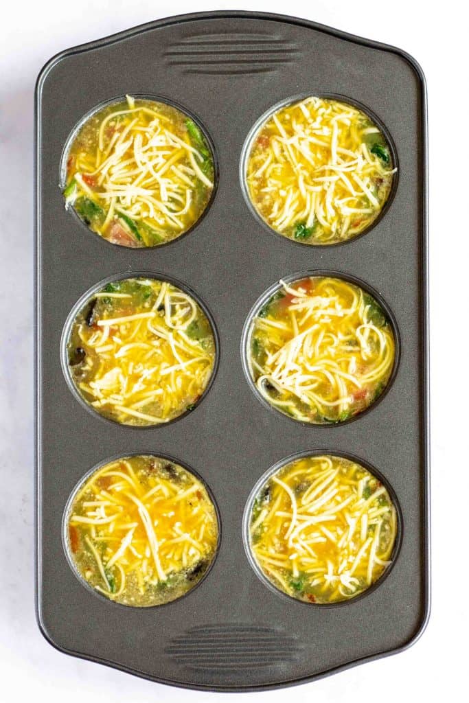 Egg mixture with cheese in muffin tin.