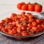 Cherry tomatoes with sprigs of fresh rosemary in a glass pie dish with additional tomatoes behind it.