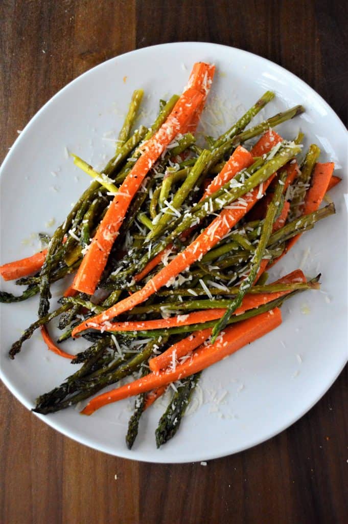 Carrots and asparagus with Parmesan cheese on a white plate.