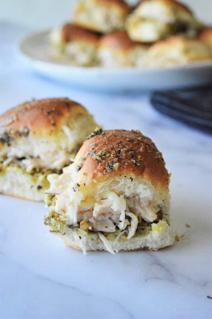 Closeup of chicken sliders on marble countertop with plate of sliders blurred in the background.