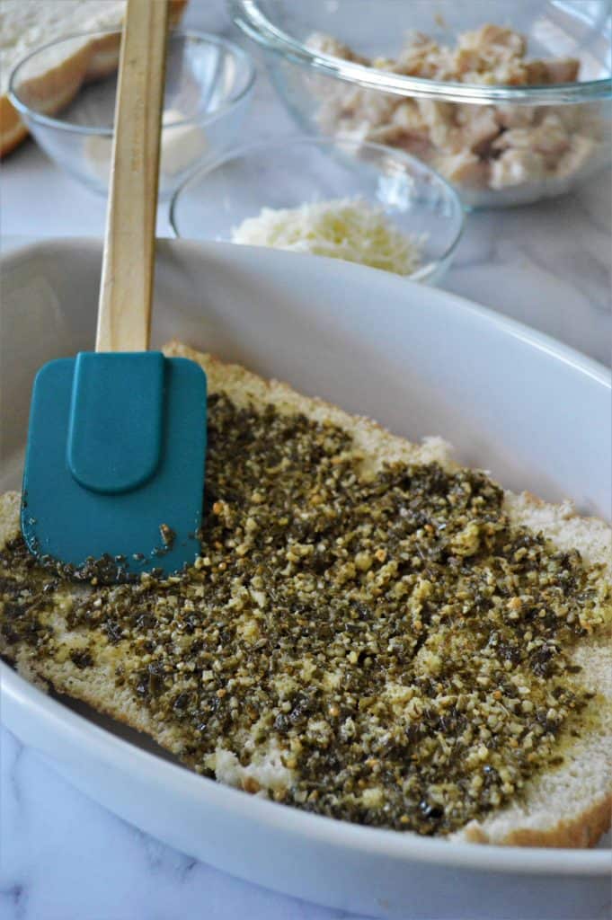 Spreading pesto with a spatula on buns.