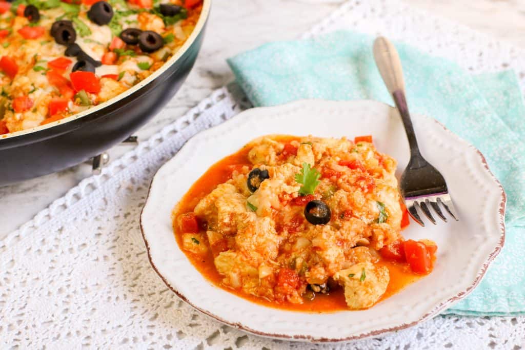 Tex Mex Chicken with Cauliflower Rice in a white bowl with a skillet of the dish behind it.
