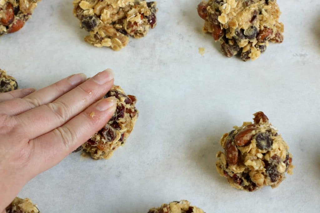 Hand pressing down cookie dough on a pan lined with parchment paper.