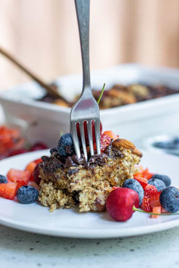 Vegan Baked Oatmeal with a fork in it and fresh berries around it on a white plate.