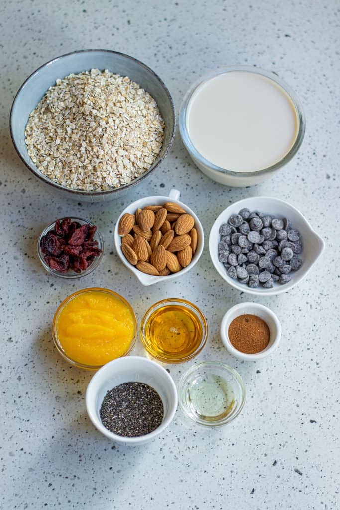 Oats, soy milk, chocolate chips, almonds, pumpkin puree and chia seeds on a countertop.