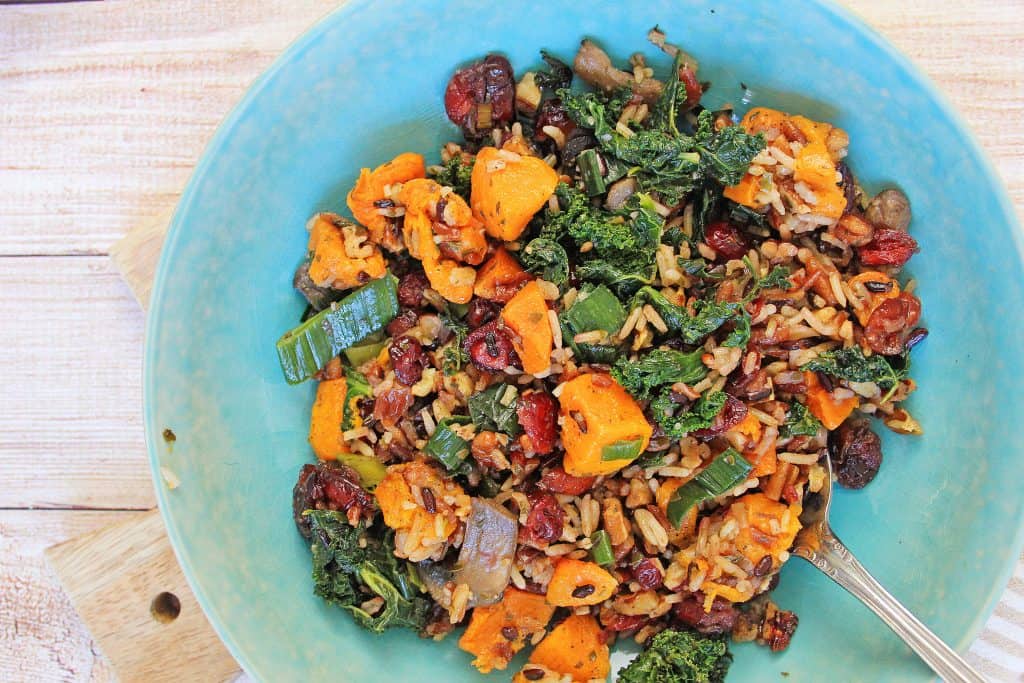 Sweet potatoes, kale dried cranberries and wild rice in a light blue bowl with a spoon in it.