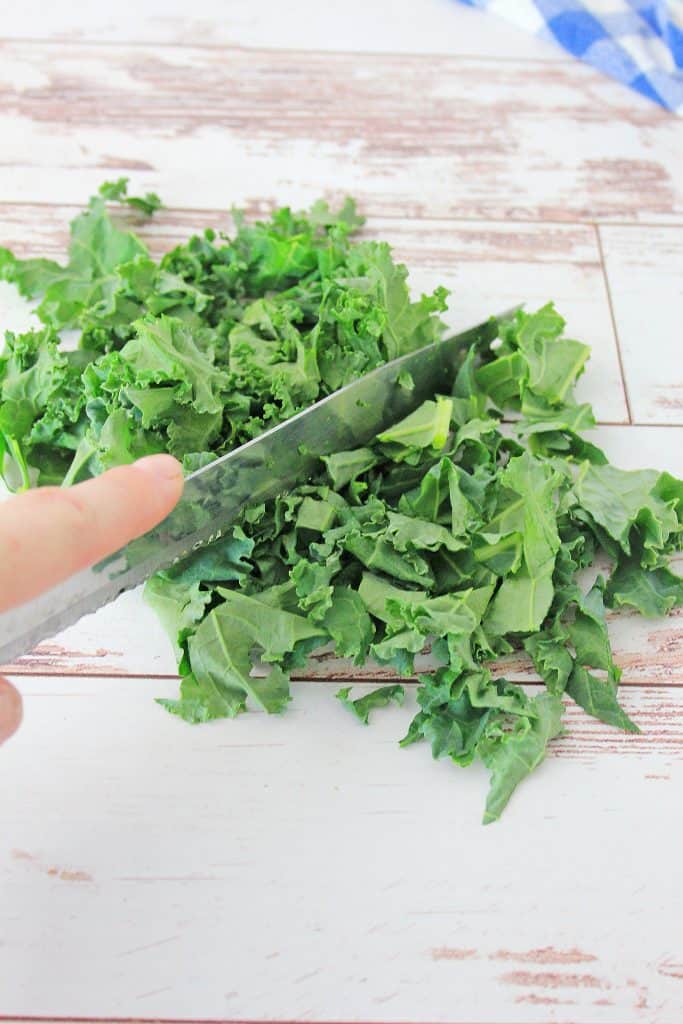 Kale being chopped on white wood cutting board.