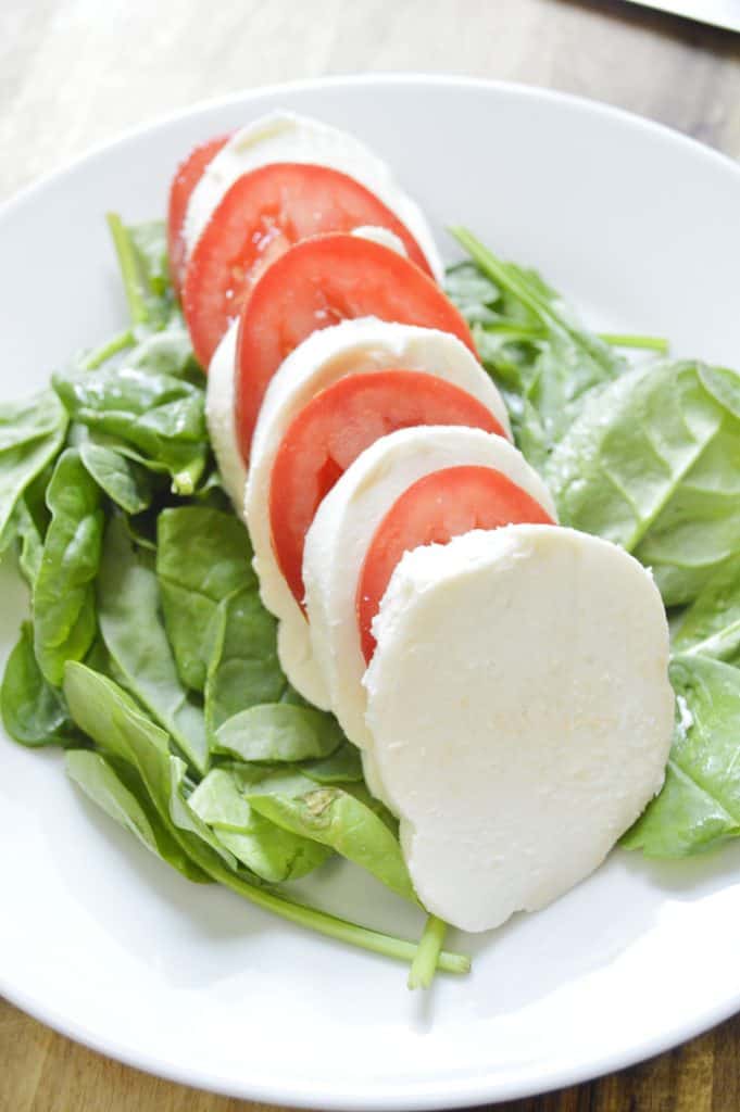 Sliced mozzarella and sliced tomato on a bed os spinach on a white plate.